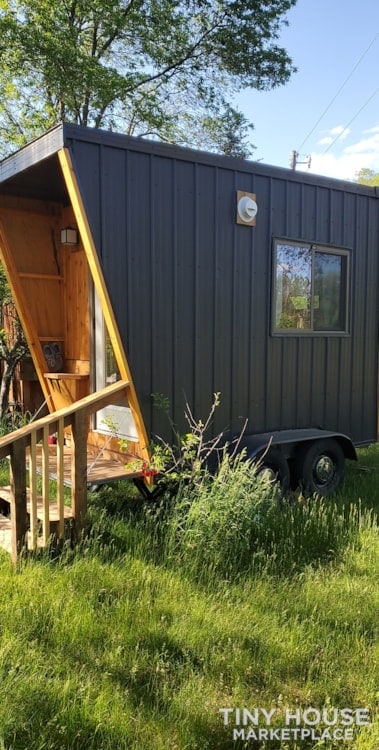 Tiny house on wheels with black exterior and small porch, ideal for mobile living and small space fr.