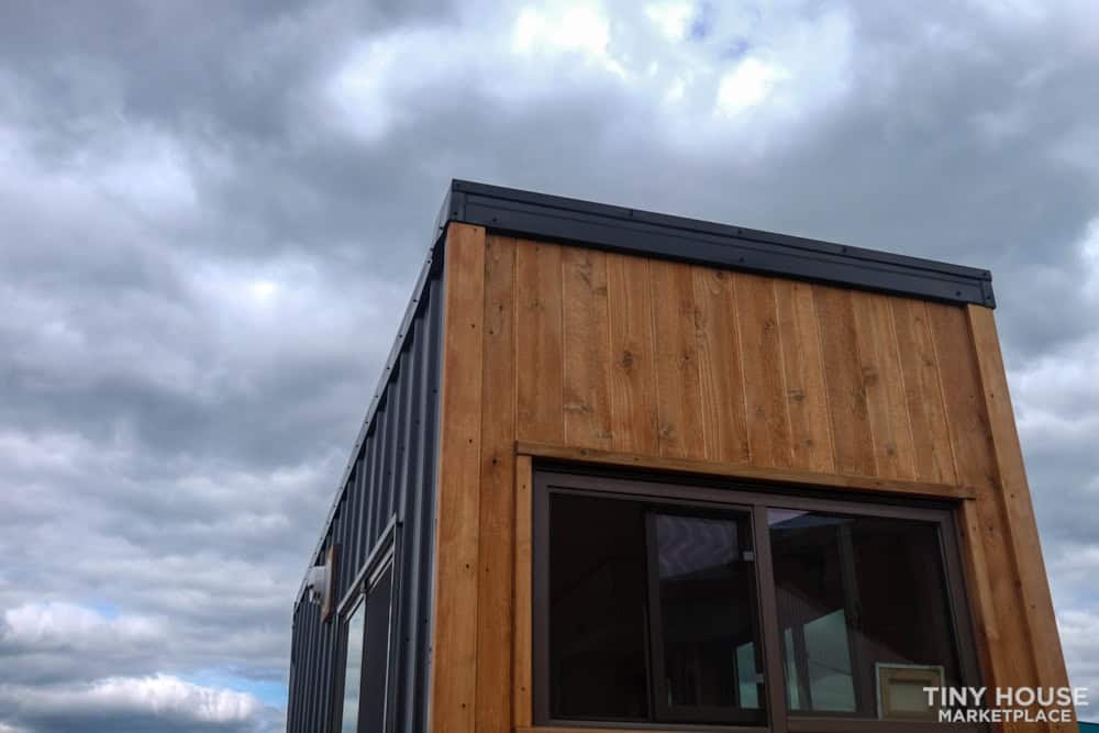 Tiny house with modern wooden exterior and large window under cloudy sky.