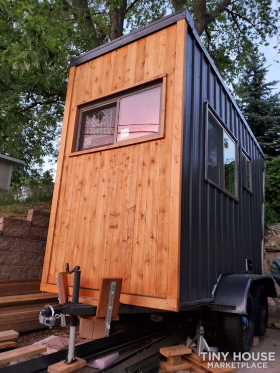 Tiny house on wheels with a modern design featuring wood and metal siding. Compact, mobile living sp.