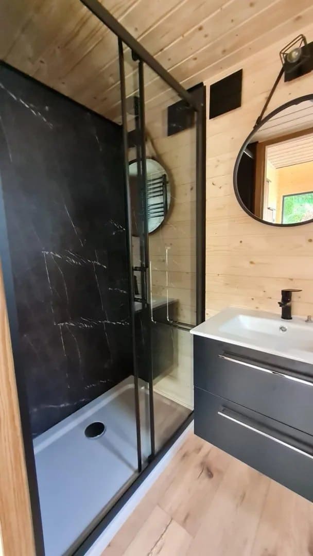 Bathroom in the Mini with a black-marble glass shower, a dark vanity, and a round mirror