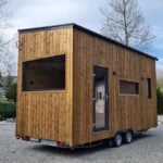 The Mini tiny house by Craft House with torched-wood siding and a single-pitch roof, on its trailer
