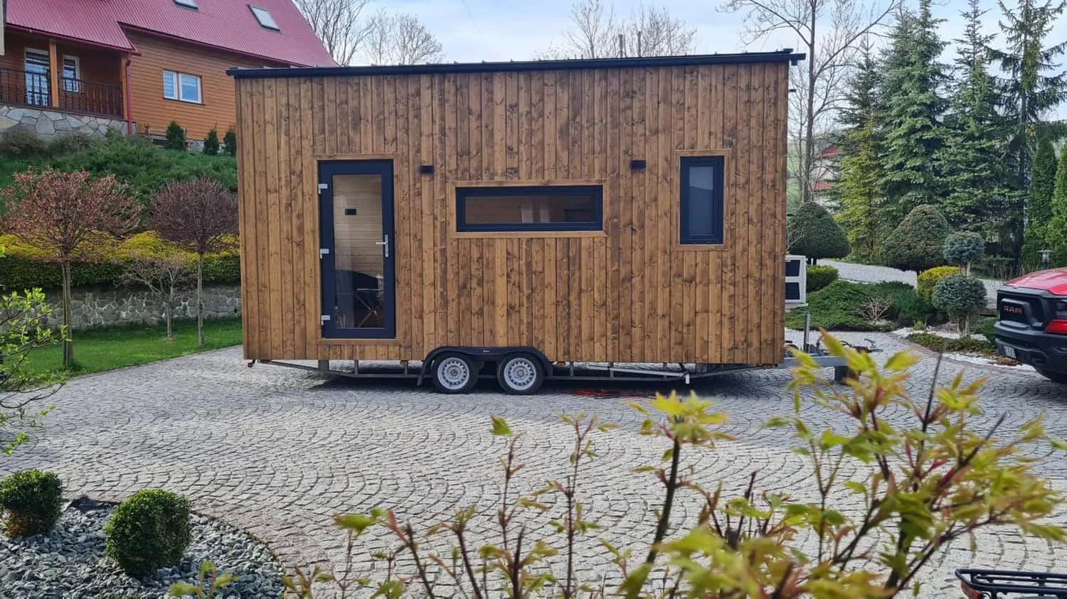 The Mini tiny house in honey-toned wood with a glass entry door and a large living-room window