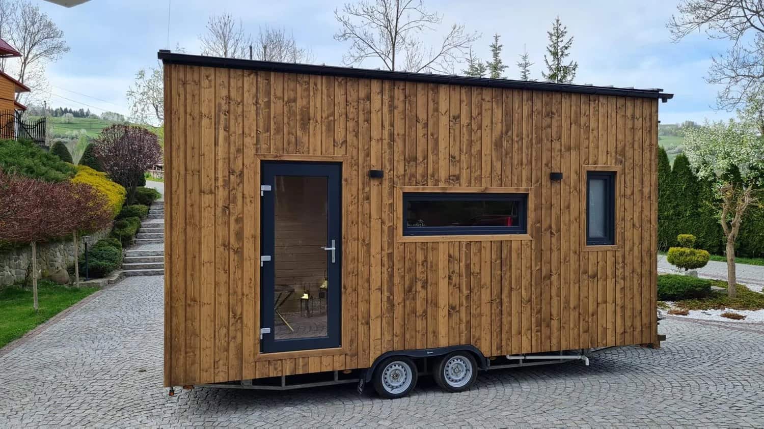 Side view of the 6-meter Mini tiny house showing the entry door, windows, and tandem-axle trailer