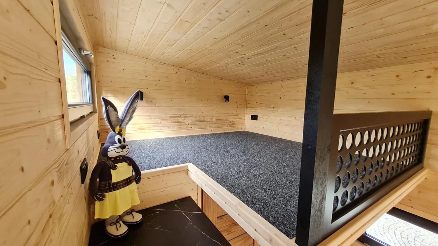 Sleeping loft in the Mini under a spruce ceiling with a black perforated guardrail