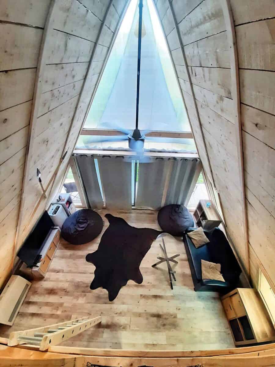 A-Frame tiny house interior with large glass window, wooden walls, and minimalist furniture.