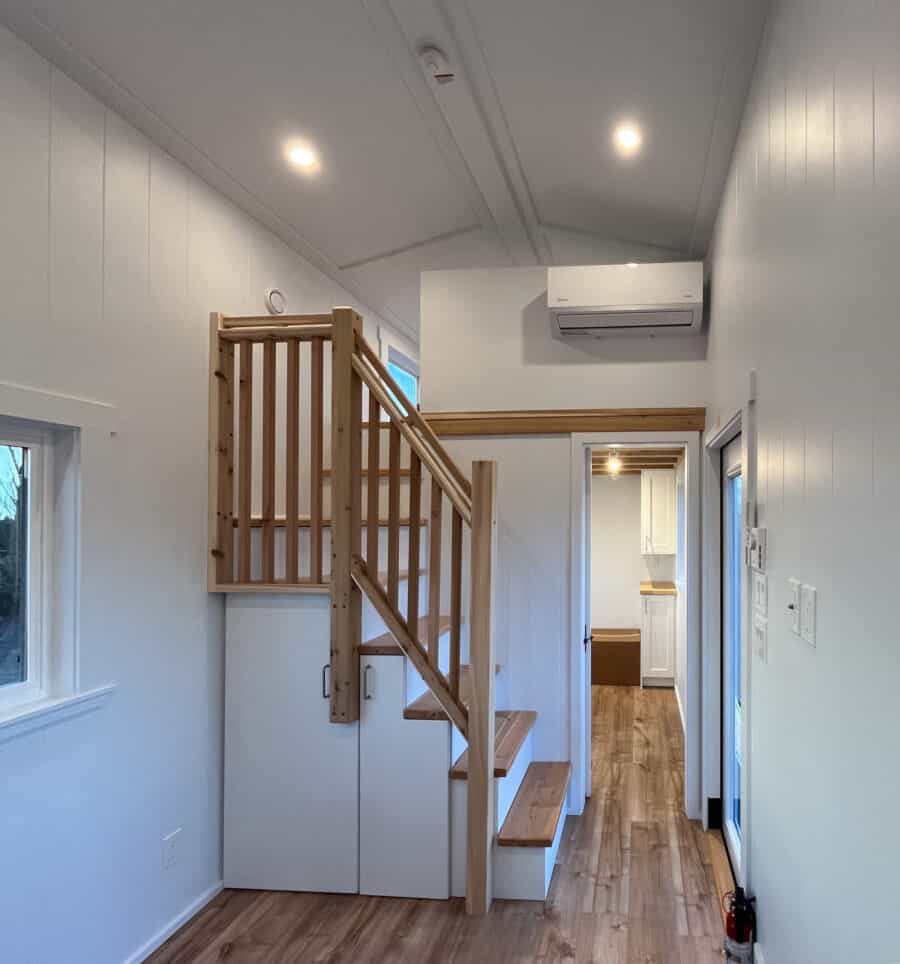 Interior view of a tiny house with wooden stairs and white walls, showcasing efficient small space d.