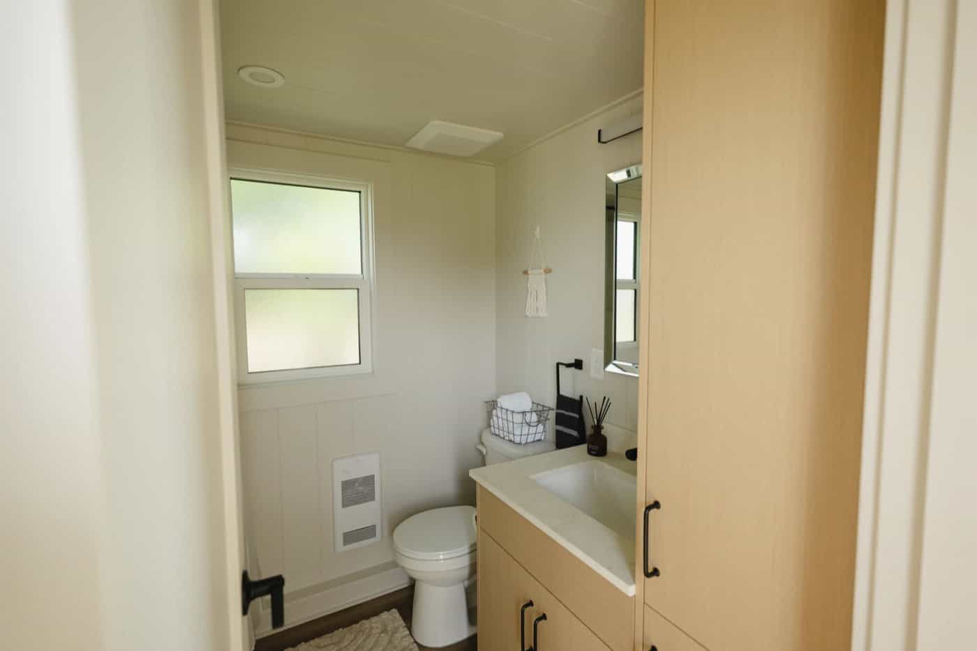 Bathroom in the Mint Ventura with a flush toilet, frosted window, wall heater, and light wood vanity