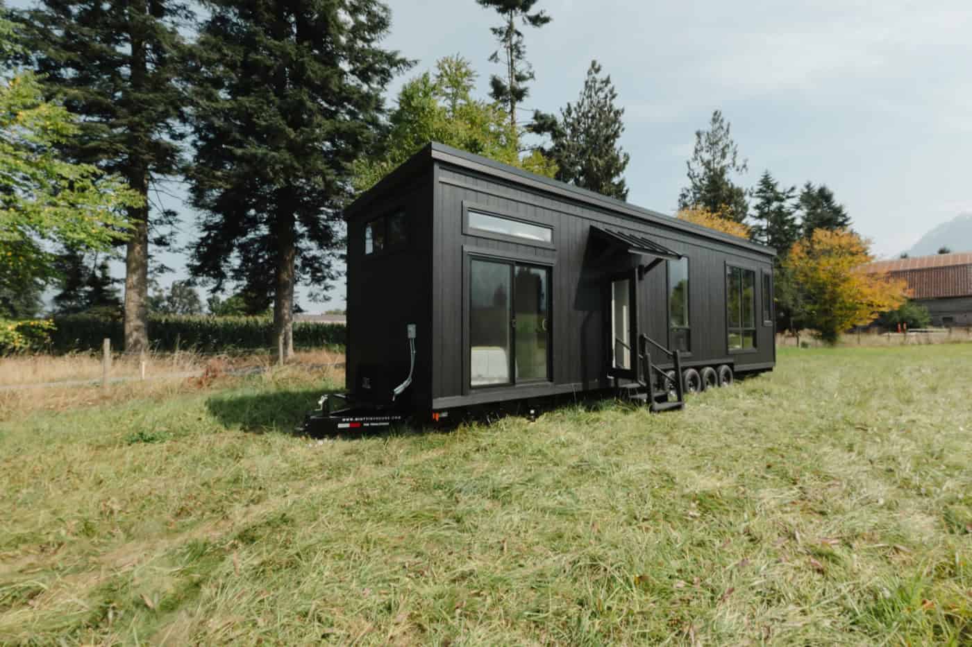 Side view of the black Mint Ventura showing its length, awning, and four-axle trailer