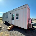 Modern farmhouse tiny house on wheels with white exterior and small steps leading to the door.