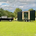 Tiny house on trailer with black and wood exterior in a green field.