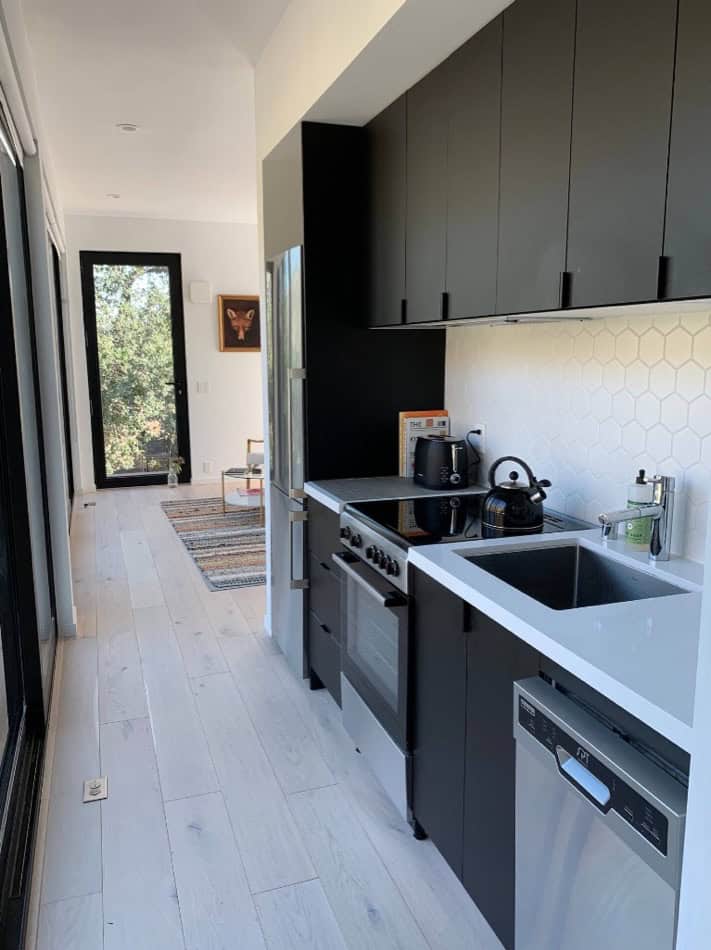 Compact modern kitchen in a canyon cabin with black cabinets and white countertops.