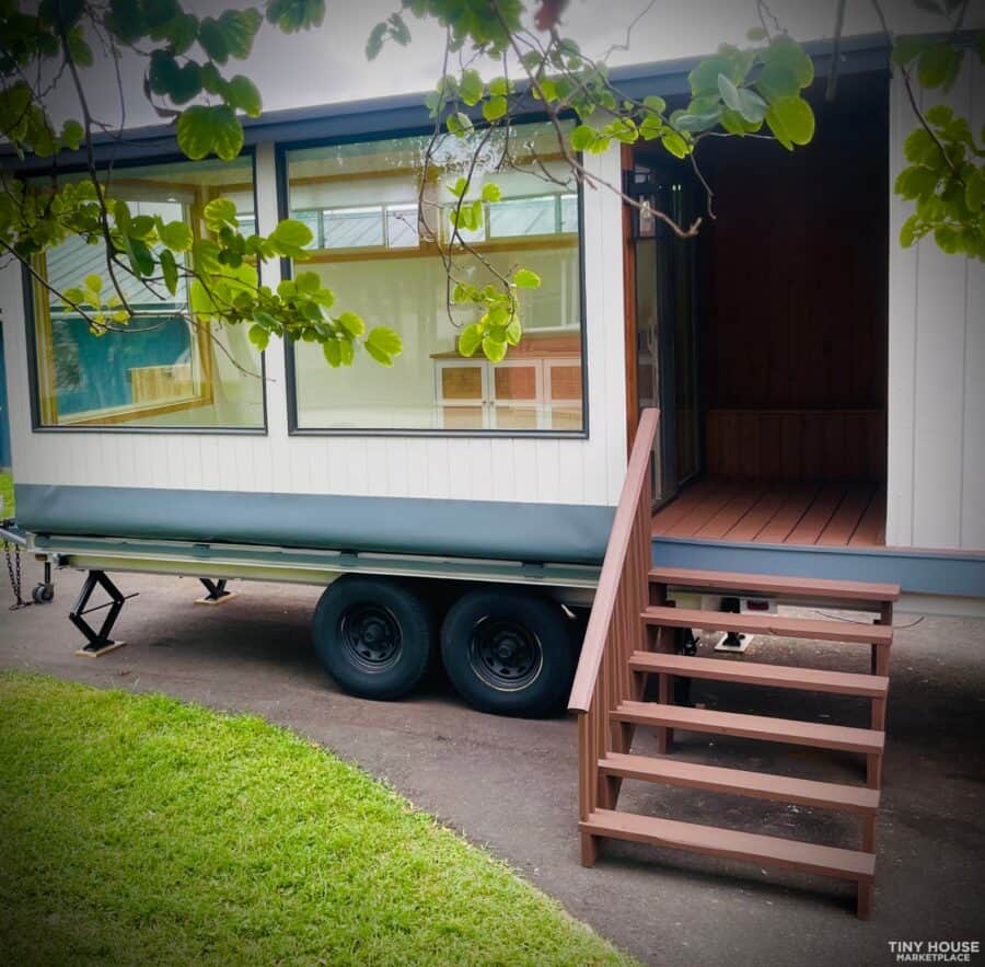 Tiny house on wheels with wooden stairs and large windows.