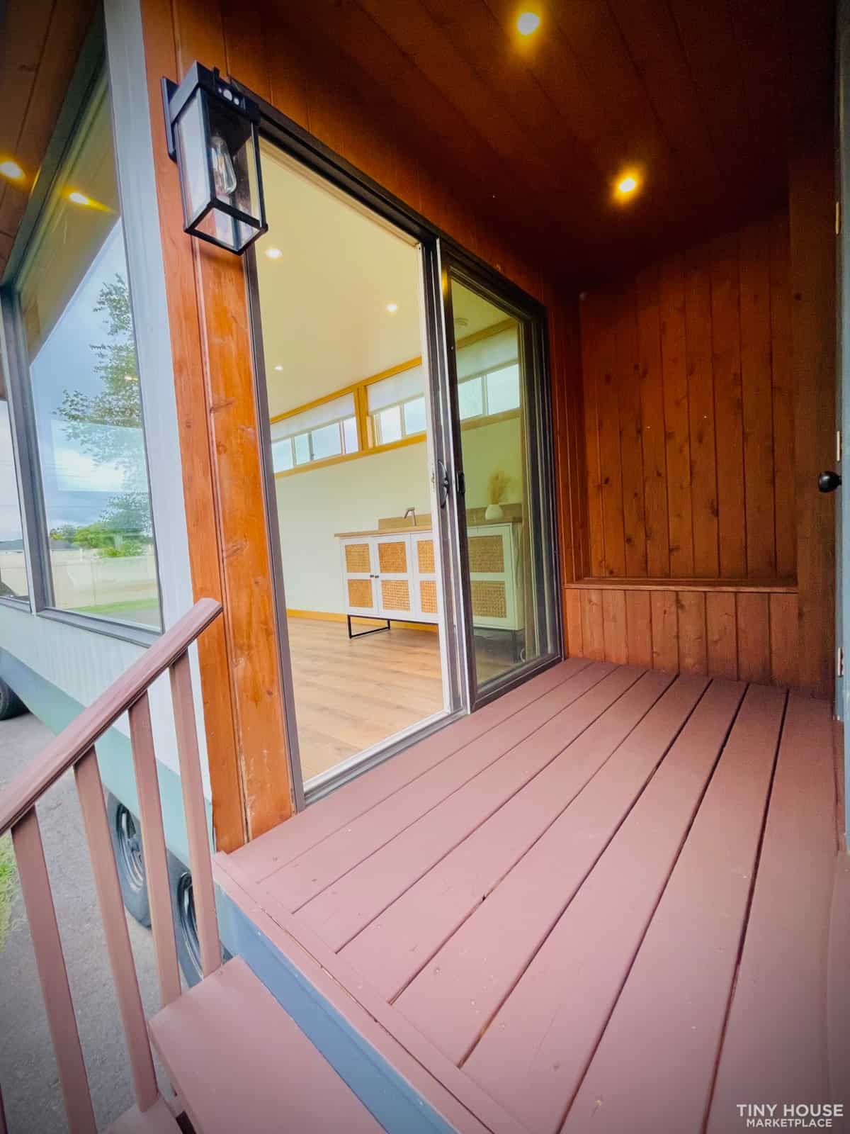 Porch of a tiny house with wooden flooring and sliding glass door.