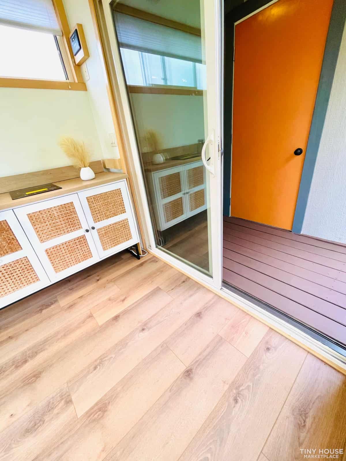Cozy tiny house interior with sliding glass door and vibrant orange door.