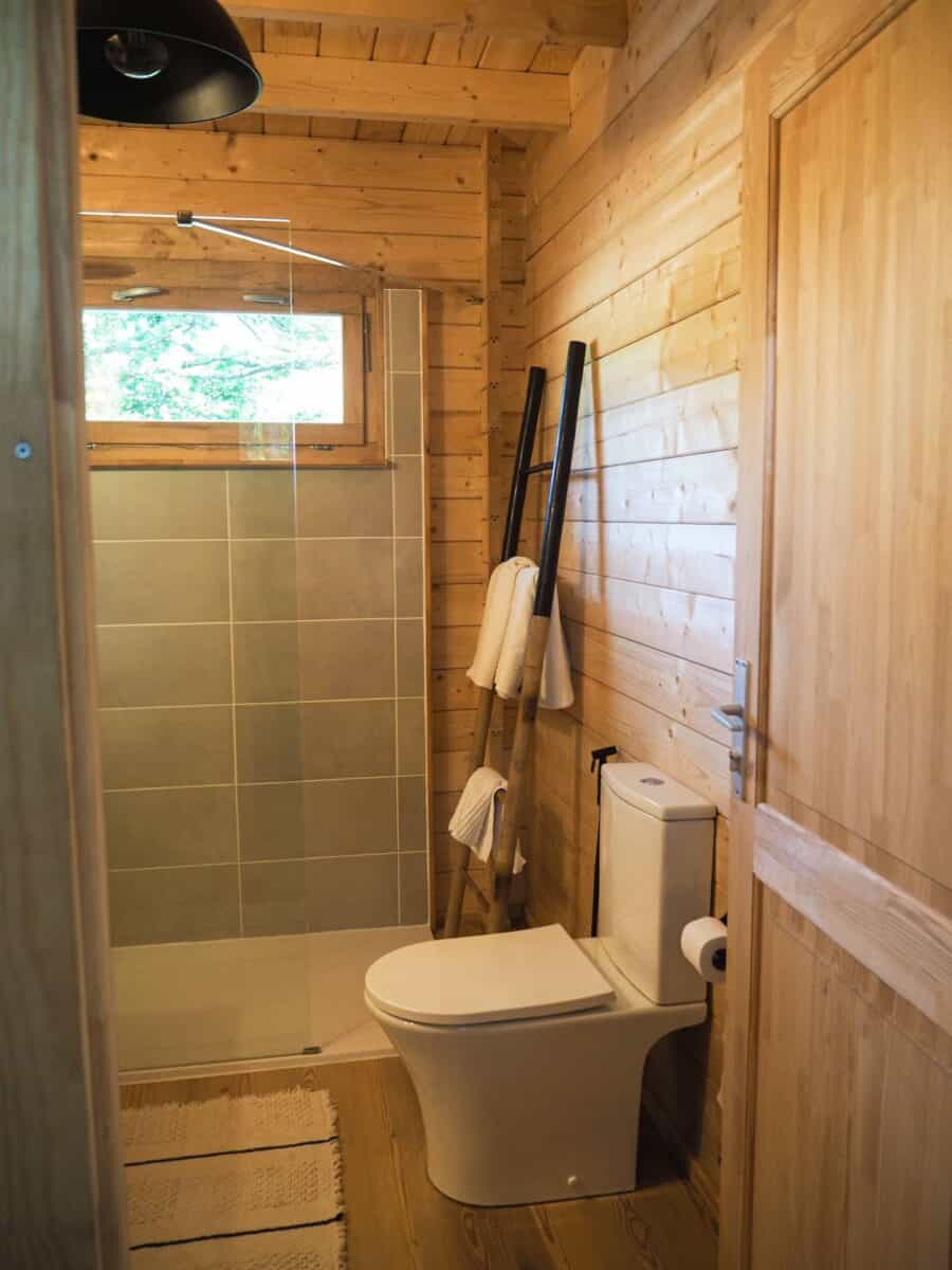 Small wooden bathroom with toilet and cleaning tools in a tiny house near hiking trails.