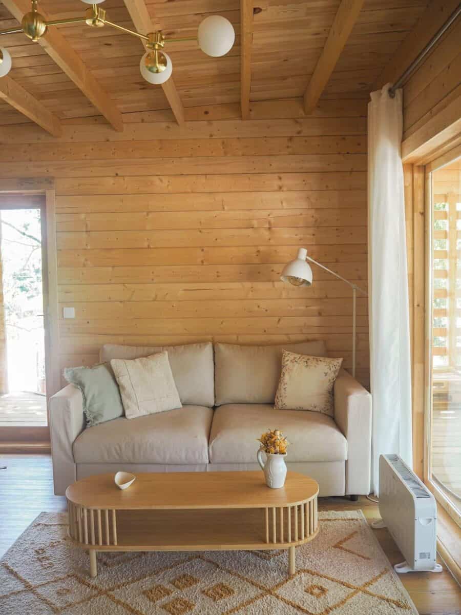 Cozy wooden interior of a small home with a beige sofa, wooden coffee table, and natural light from.