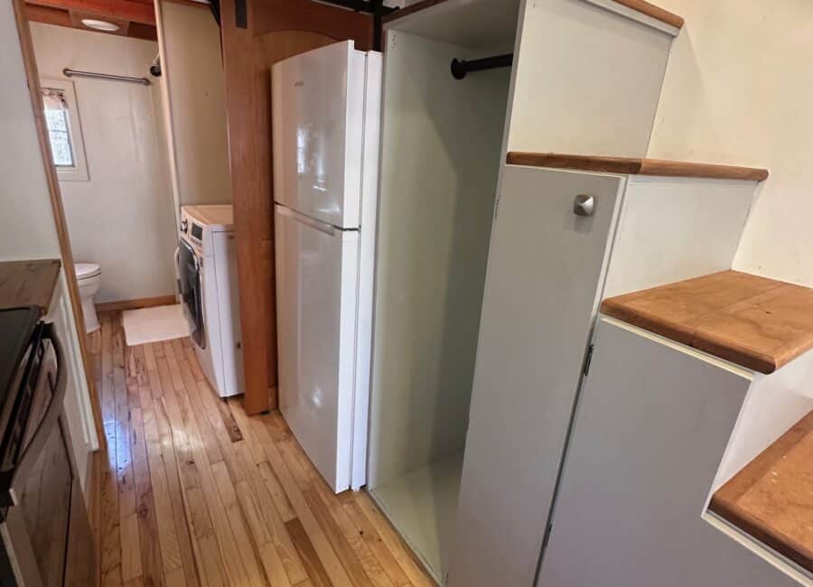 Compact tiny house kitchen with fridge, washer, and storage cabinets.