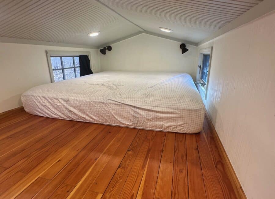 Compact tiny house bedroom with sloped ceiling and natural light.