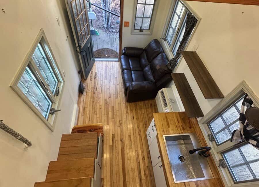 Compact tiny house interior with a small living area and kitchen. Bright windows offer scenic creeks.