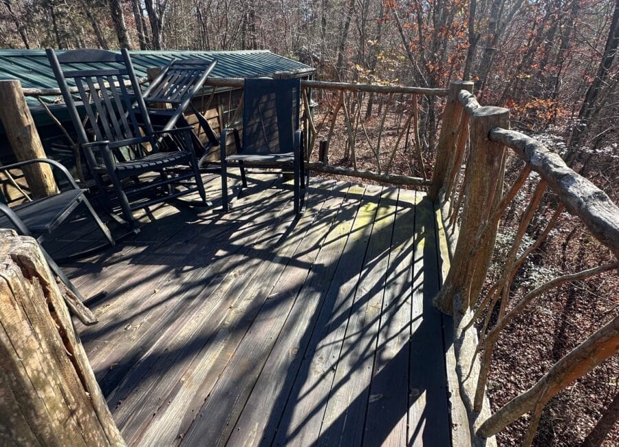 Deck overlooking a creek with rustic wooden railing and outdoor seating.