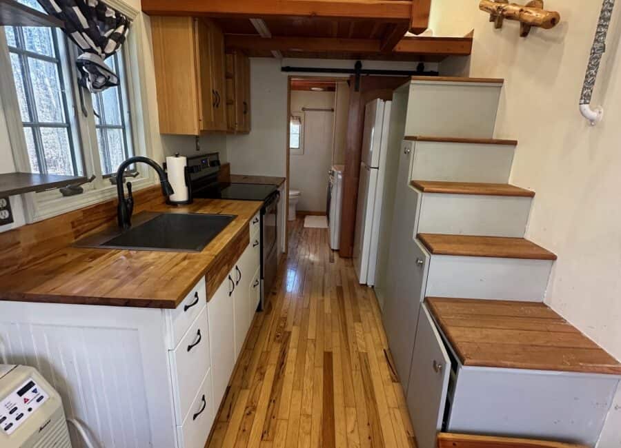 Compact tiny house kitchen with wooden countertops and cabinetry, maximizing small space efficiency.