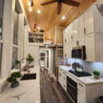 Modern tiny house kitchen with loft, white cabinets, and wooden ceiling.