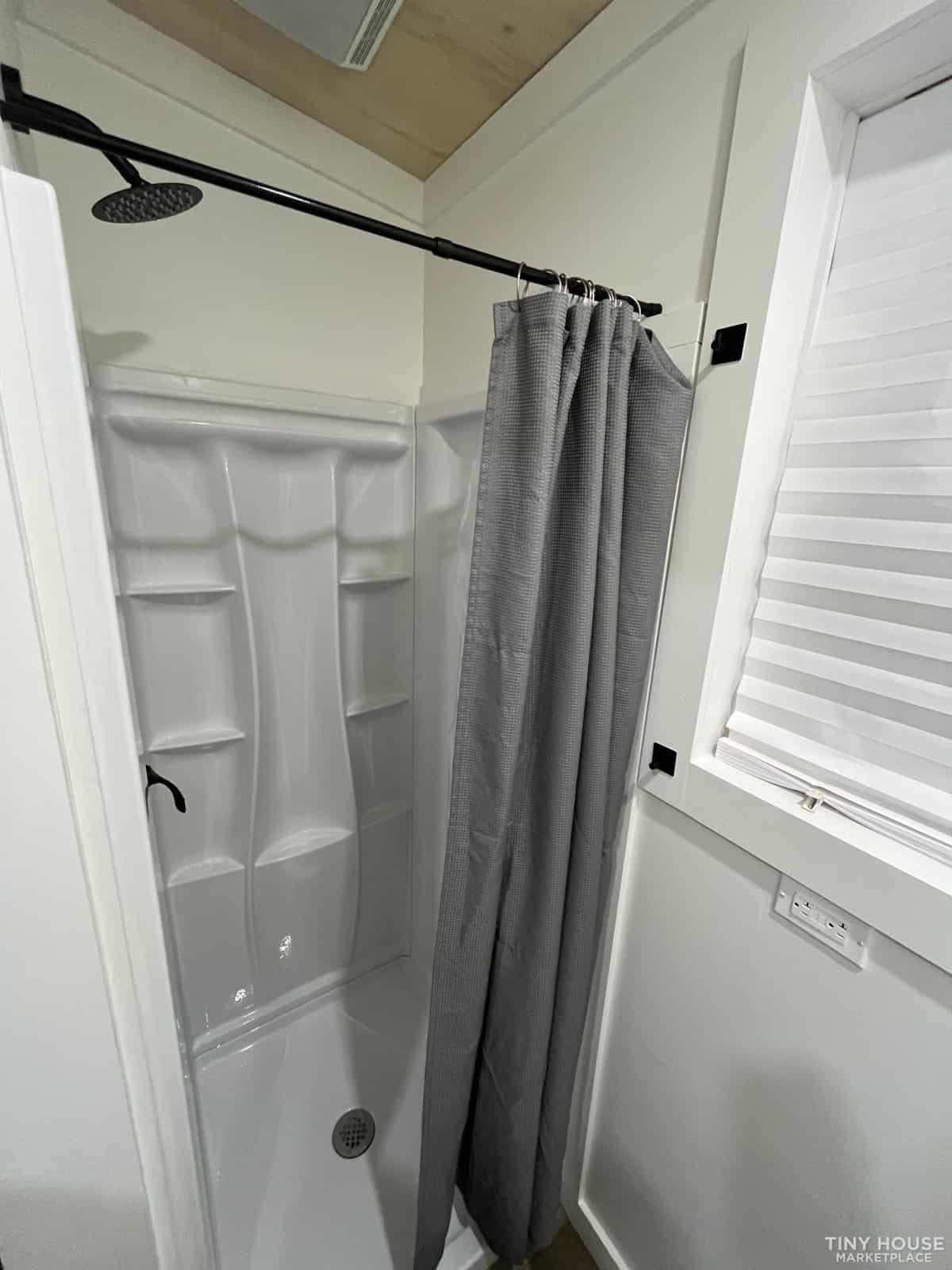 Compact shower with gray curtain in tiny house bathroom.