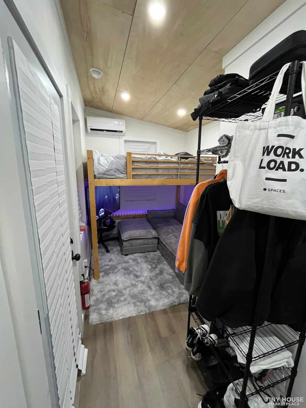 Compact tiny house bedroom featuring a bunk bed, organized clothing rack, and efficient use of space.