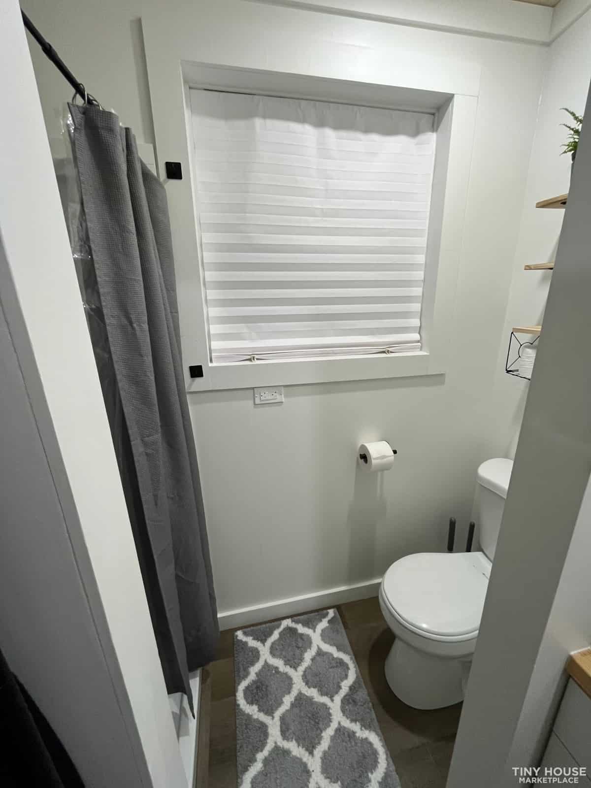 Small bathroom with window, toilet, and shower curtain in tiny house.