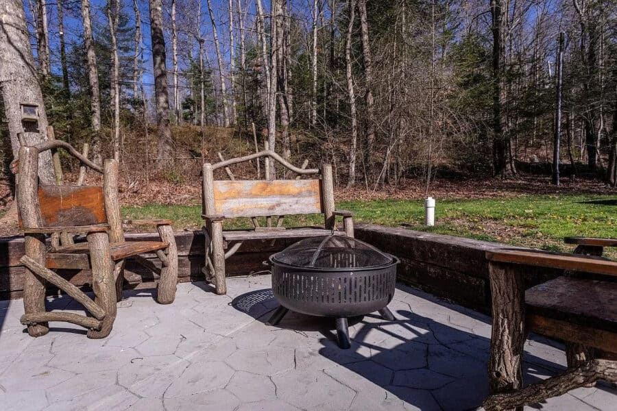 Rustic outdoor seating area with fire pit in wooded setting.