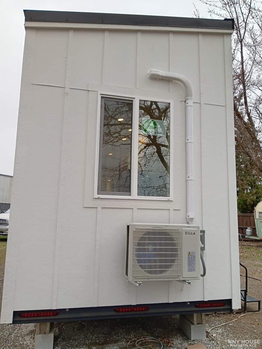 Small tiny house exterior with HVAC unit and window, on wheels for mobility.