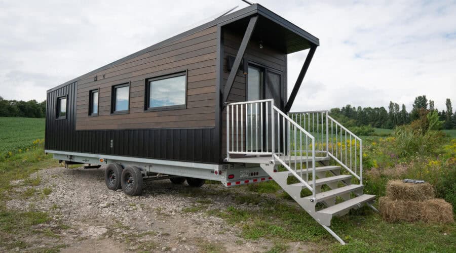 Modern 30-foot tiny house on wheels with sleek exterior, set in a natural landscape.