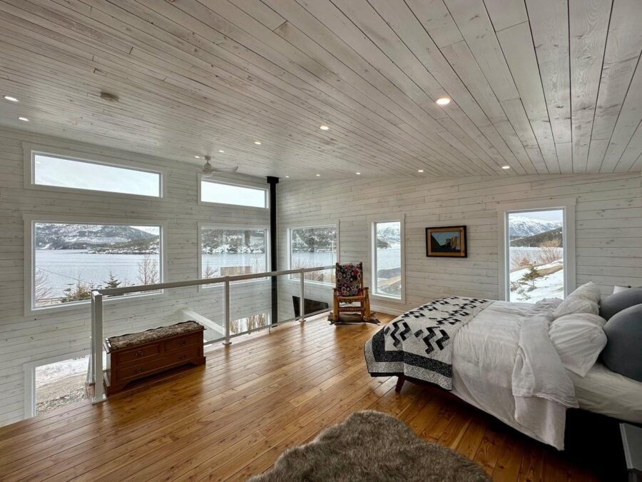 Bright cabin bedroom with large windows overlooking snowy lake scenery.