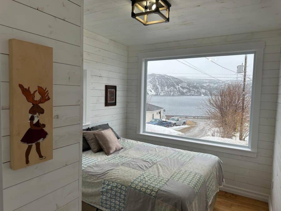 Cozy tiny house bedroom with large window overlooking snowy landscape and lake.