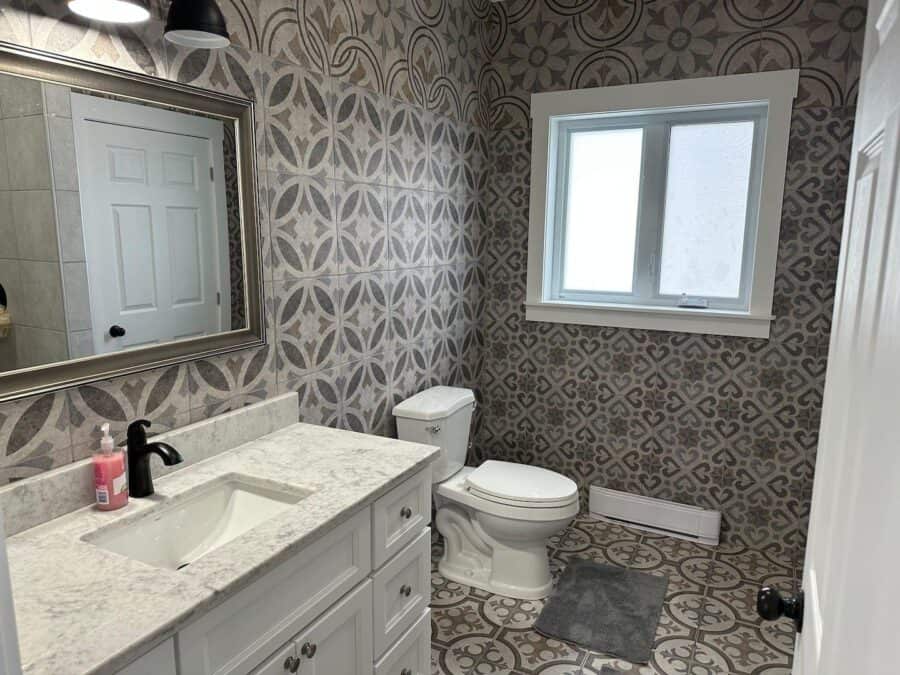 Small bathroom with patterned wallpaper, white vanity, and window in Nora’s Nook cabin.