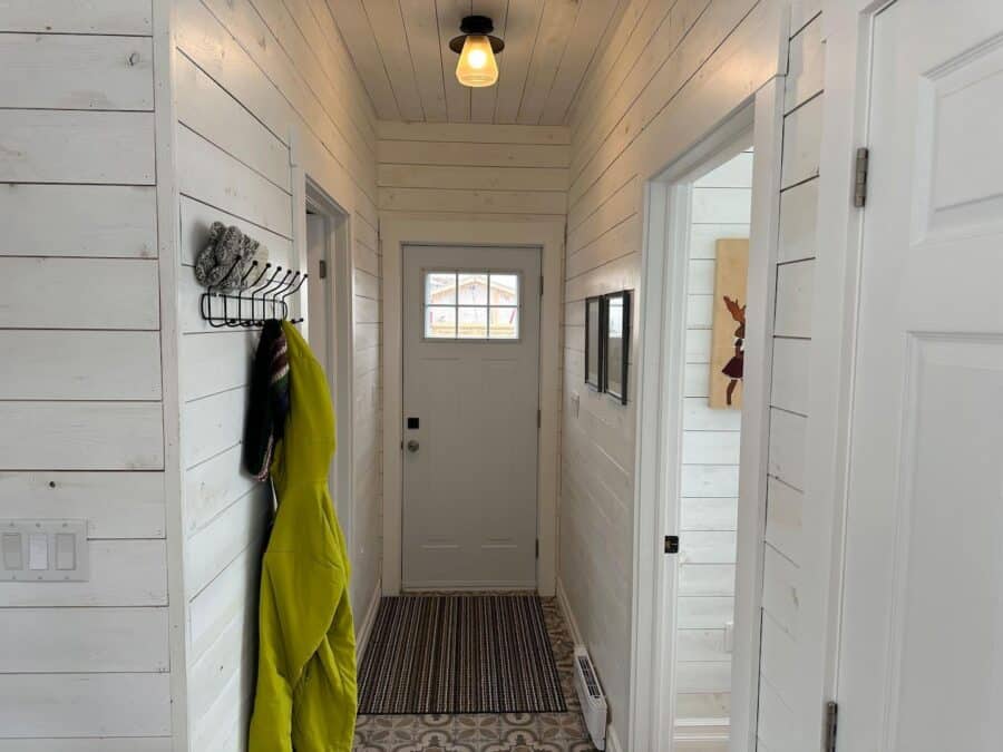 Small cozy cabin entryway with white wooden walls and a striped rug.