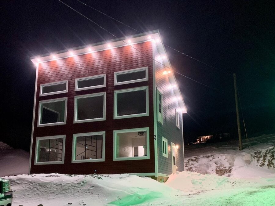Tiny house with festive string lights in a snowy landscape.