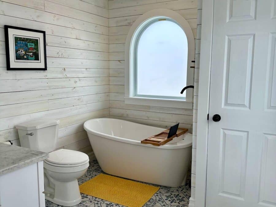 Charming tiny house bathroom featuring a white freestanding tub, toilet, and natural light from a la.