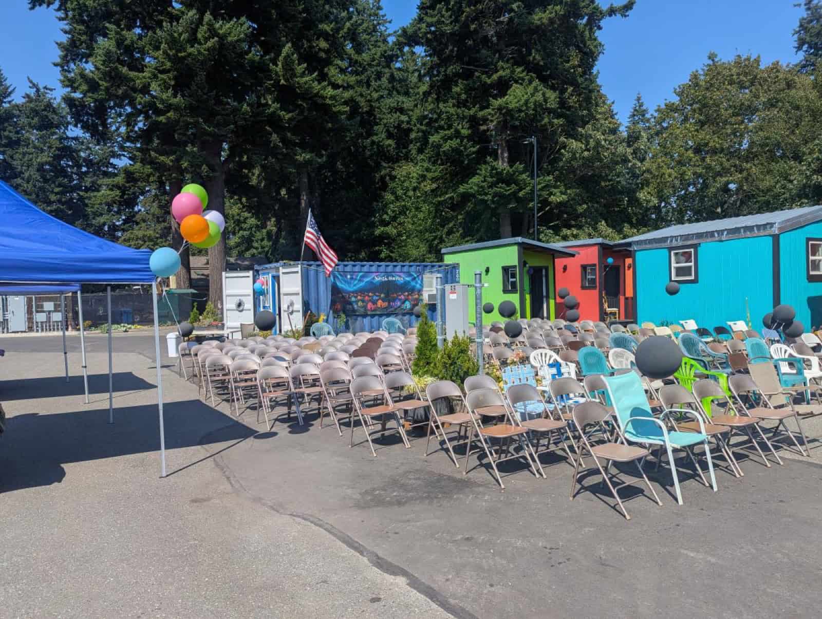 Crowd seated among colorful tiny homes beneath a North Haven banner at the village opening celebration