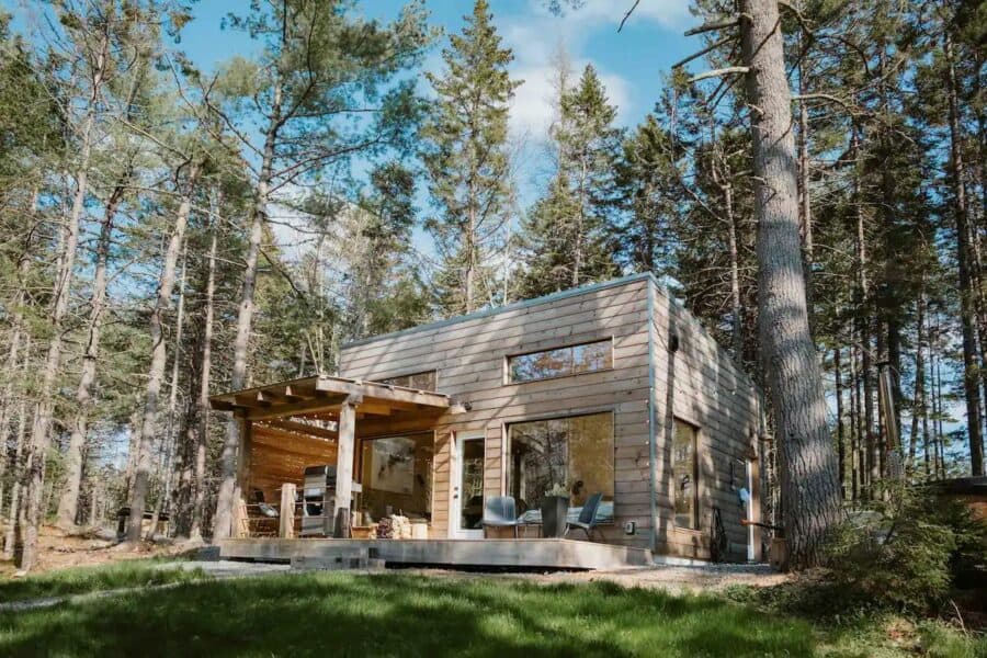 Charming tiny house nestled among tall trees in Nova Scotia, featuring a wood-fired hot tub for rela.