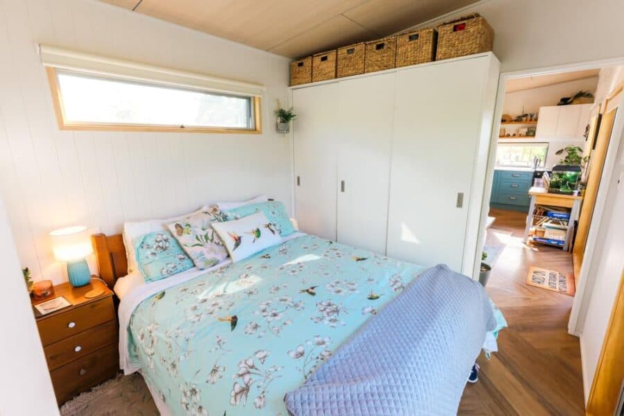 Cozy tiny house bedroom with large window, white walls, and built-in storage.