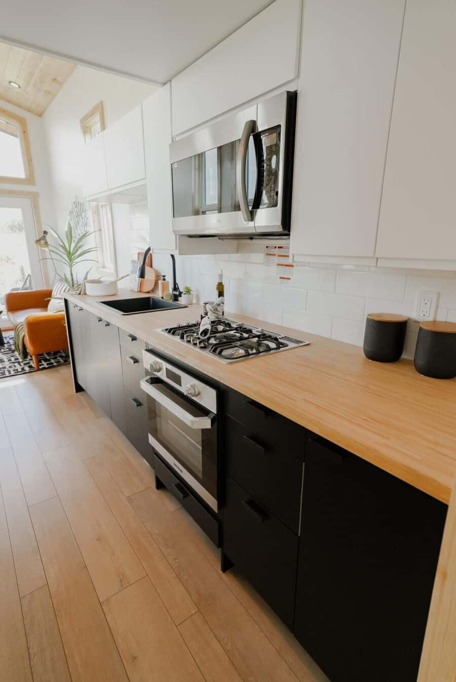 Compact tiny house kitchen with built-in microwave, stove, and sleek cabinetry.