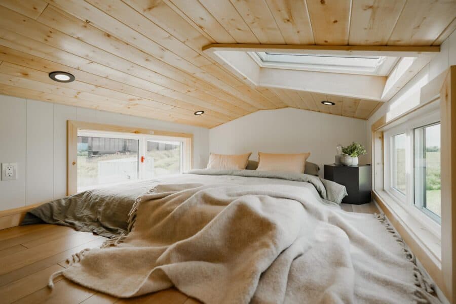 Cozy tiny house bedroom featuring natural wood accents and a skylight for bright, airy living space.
