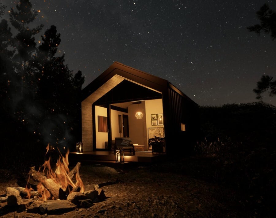 Modern tiny house at night with cozy interior lighting under a starry sky.