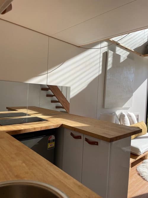 Bright tiny house kitchen with wooden countertops and modern appliances under skylight.