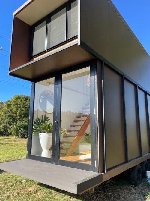 Contemporary two-story tiny house with sleek black exterior and large glass windows.