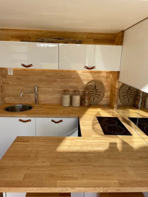 Compact tiny house kitchen with modern white cabinets and wooden accents.