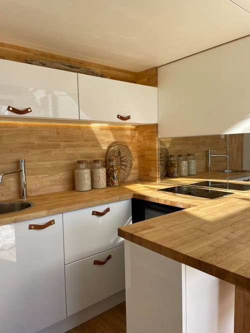 Compact tiny house kitchen featuring sleek white cabinets and warm wooden countertops.