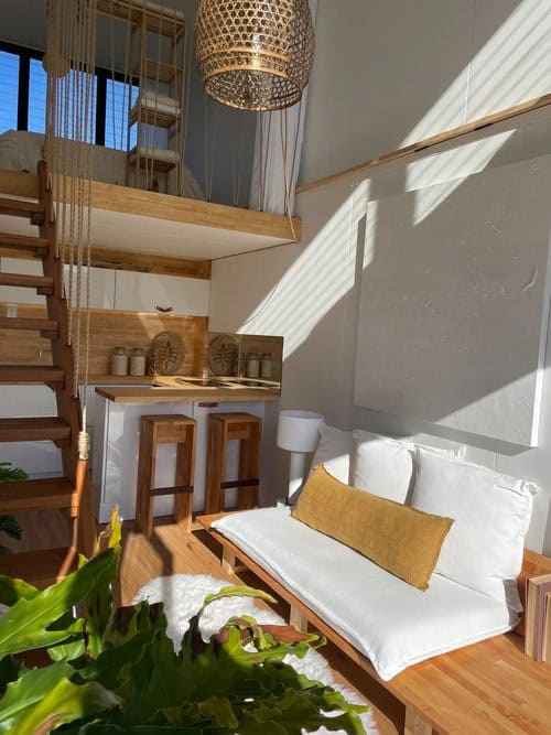 Bright tiny house interior with loft, wooden furniture, and natural sunlight.