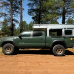 Green pickup truck with a camper in a forest setting.